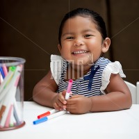 Little girl smiling and holding markers on white table