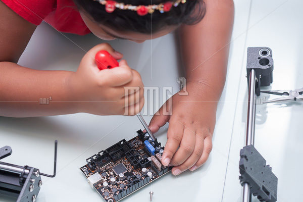 Little hands of a smart kid working on electronic device with a screw driver on hand and other components for summer camp