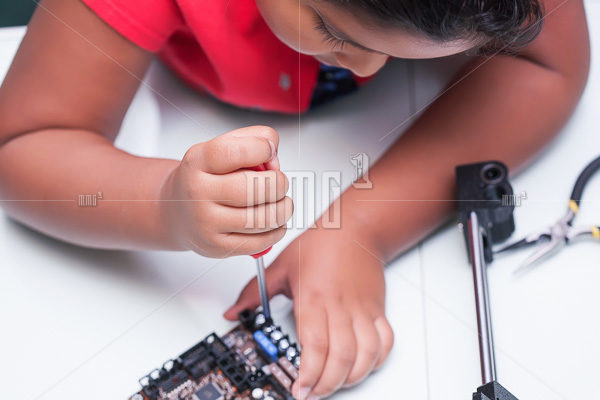 Young child learning about electronics and technology by wiring and holding screw driver making a connection in class